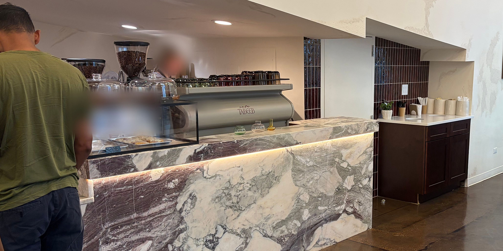 A finished cafe service counter in veined marble, lit from beneath the lip, with the espresso bar and pastry case behind it