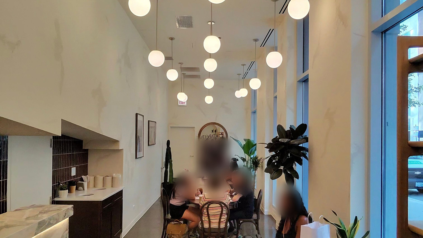 A finished cafe interior: a marble service counter, a row of globe pendants down a double-height room, an arched mirror and planting