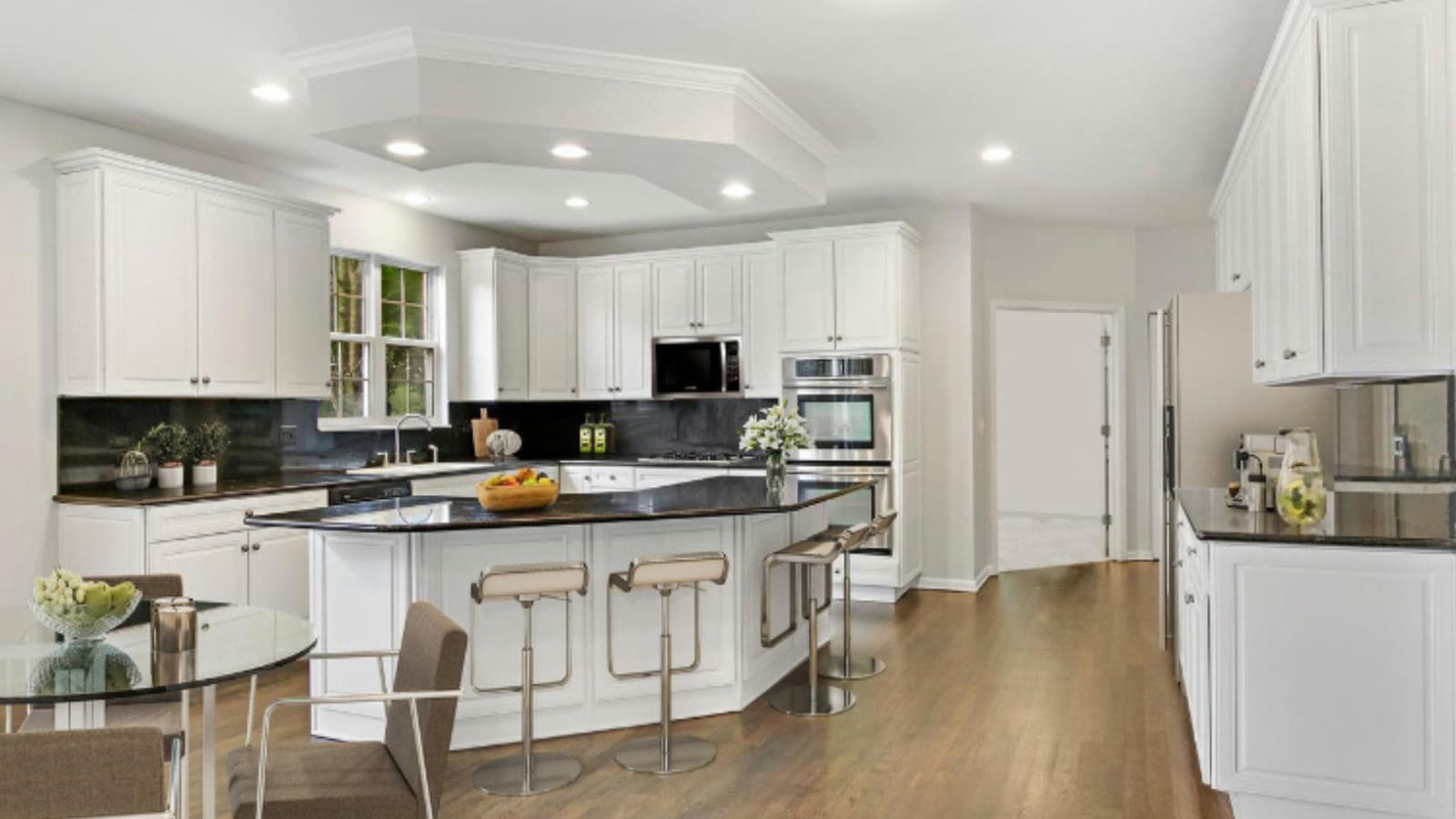 A finished kitchen in white with a stone-topped island, stools and stainless appliances