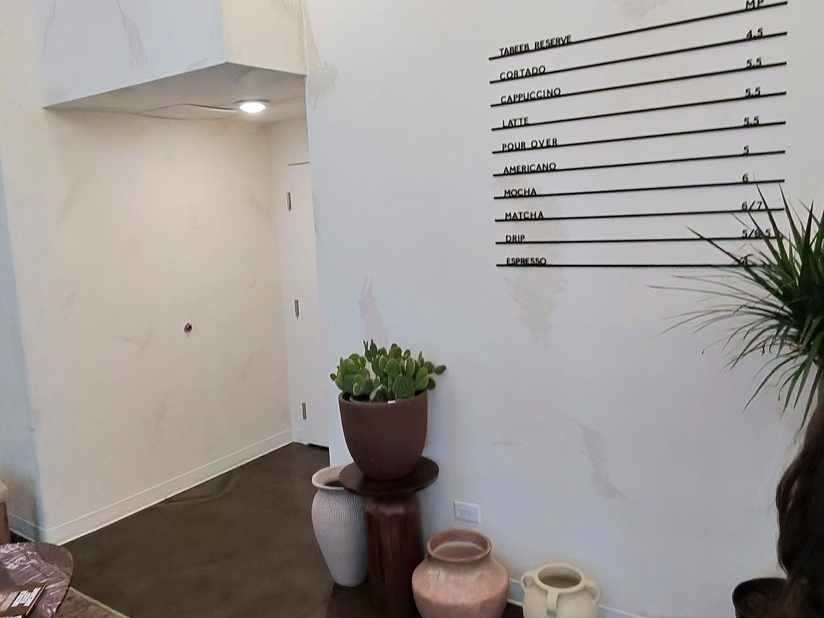 A quiet corner of a cafe: hand-troweled plaster walls, a wall-mounted menu board, and pottery grouped on a polished concrete floor