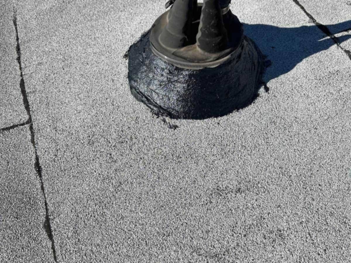 A pipe penetration on a flat roof, sealed with black roof cement over a granulated cap sheet