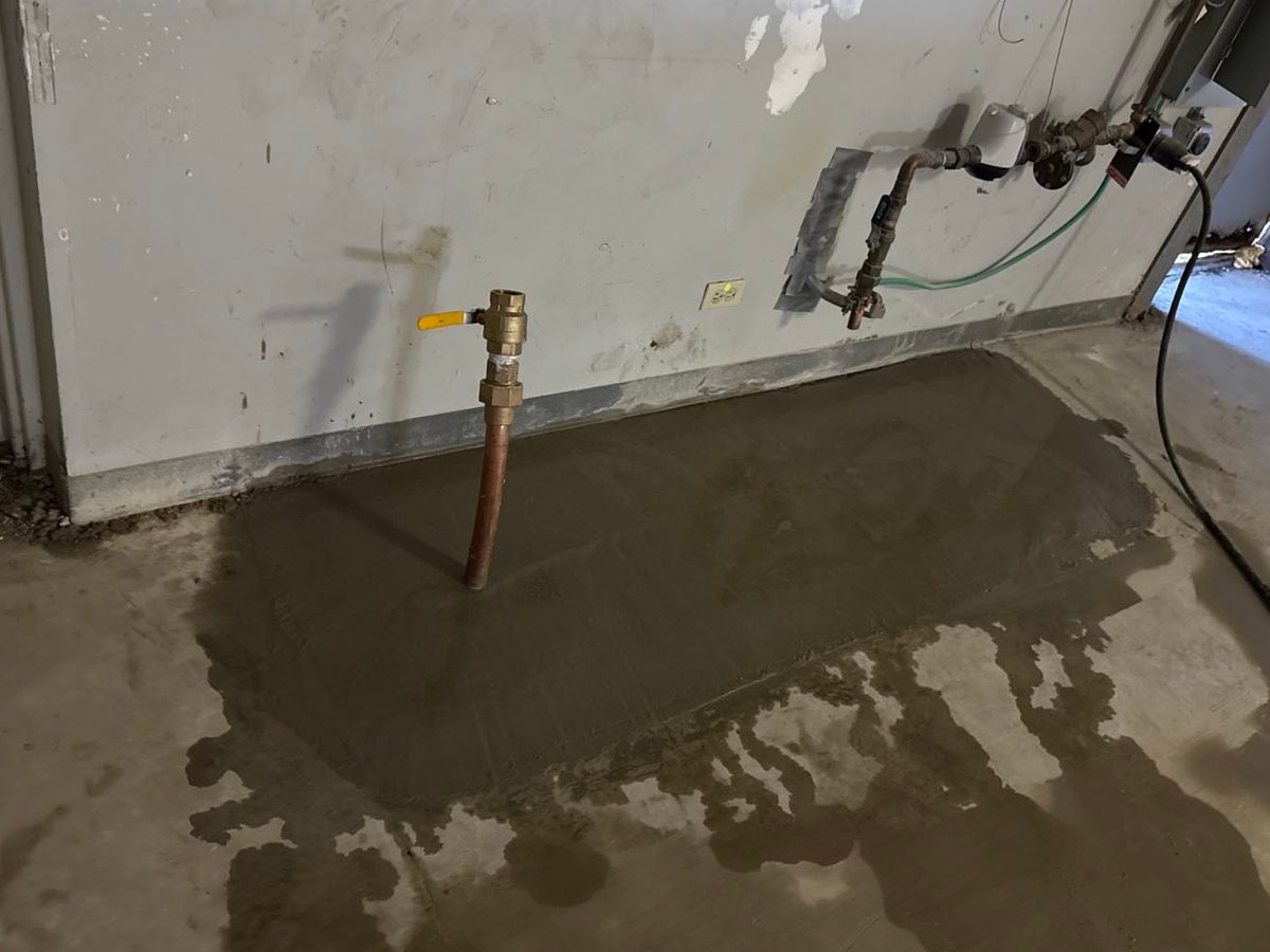 A utility room with a freshly poured floor patch over a trenched line