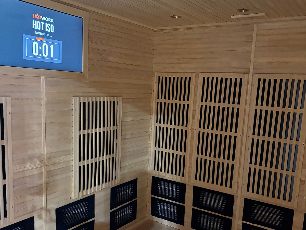 Inside an infrared room: pale cedar lining, slatted heater panels along two walls, and a wall screen counting down to a session