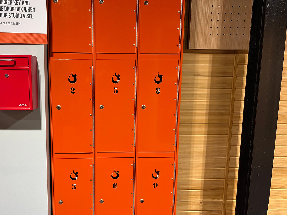 A bank of orange lockers numbered two to nine, beside a red key drop box and a cedar-clad wall