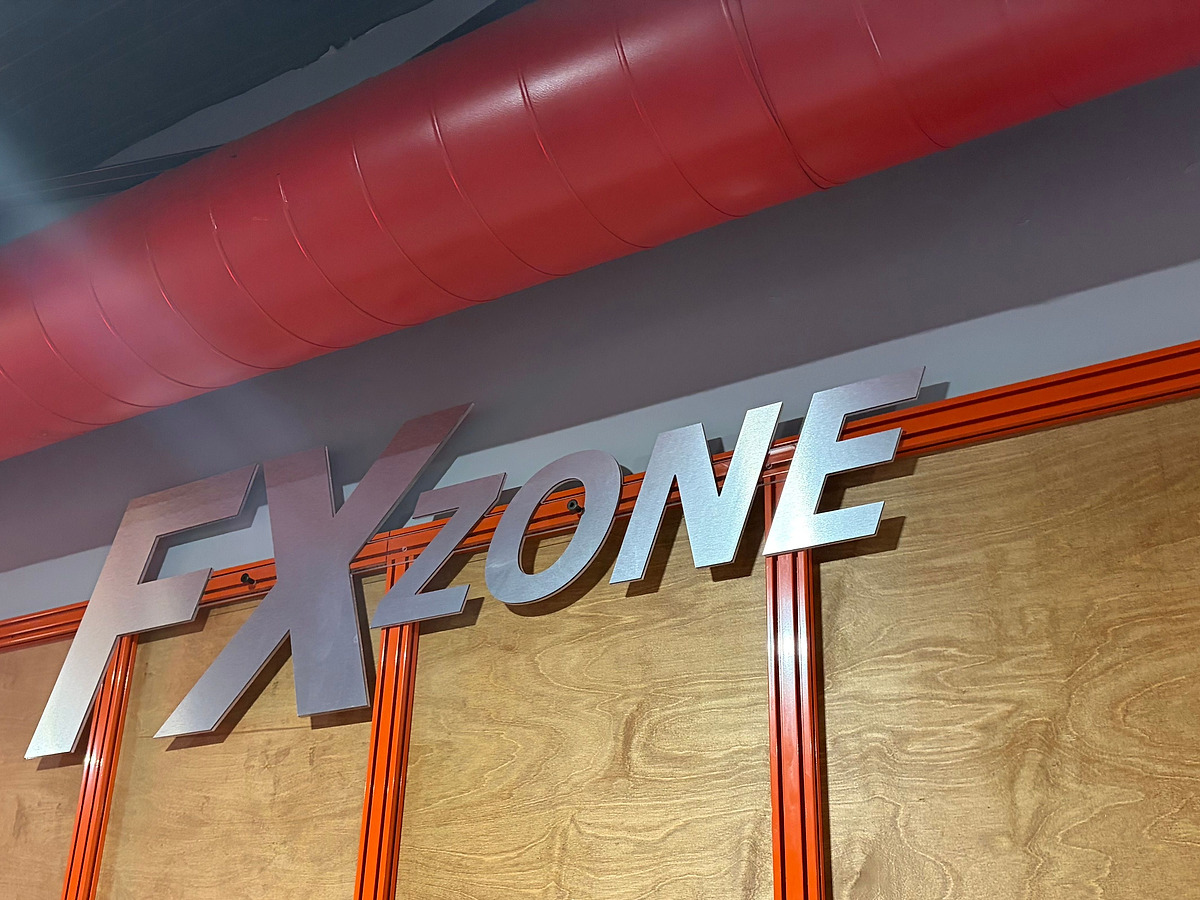 FX ZONE in brushed dimensional letters on a plywood and orange steel wall, under a red spiral duct
