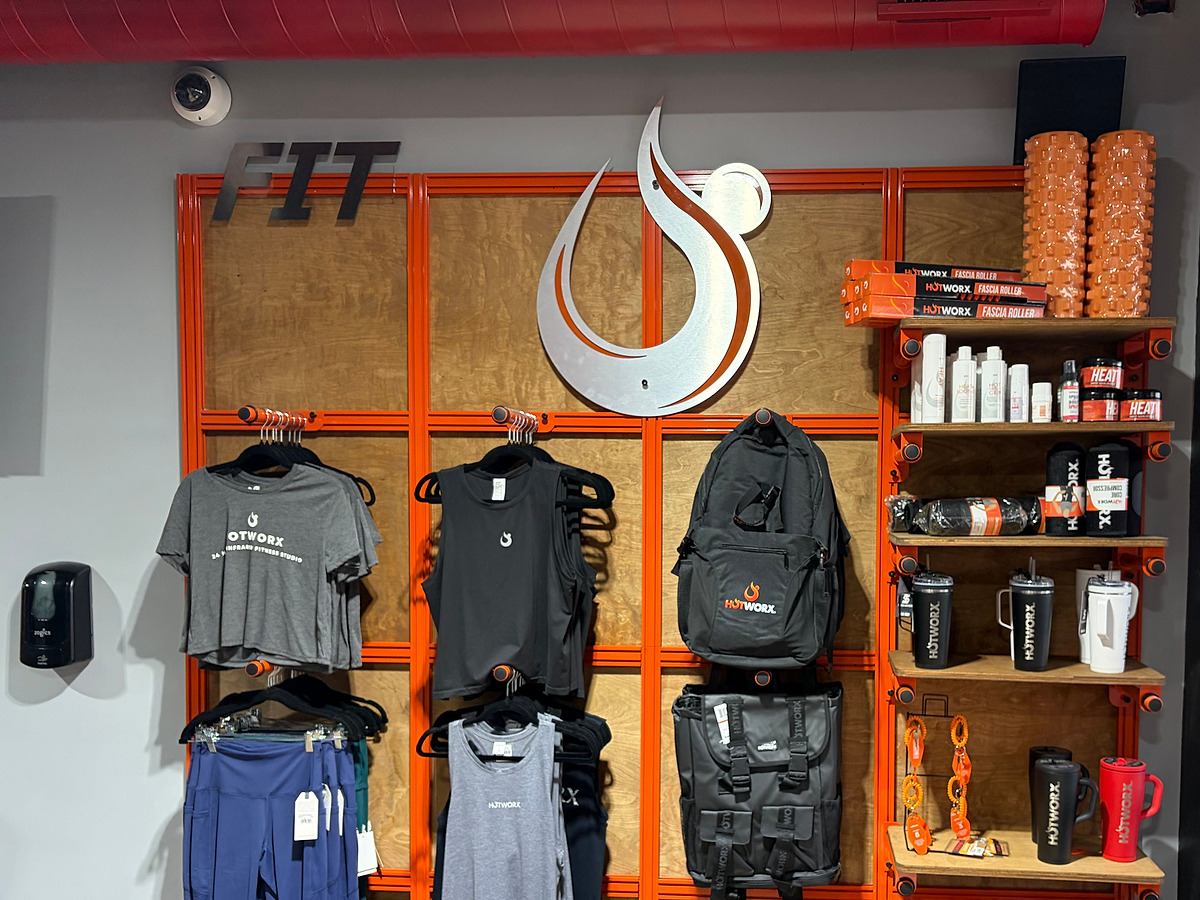 A retail wall on the same plywood and orange steel grid, hung with apparel and shelving under a brushed flame sculpture