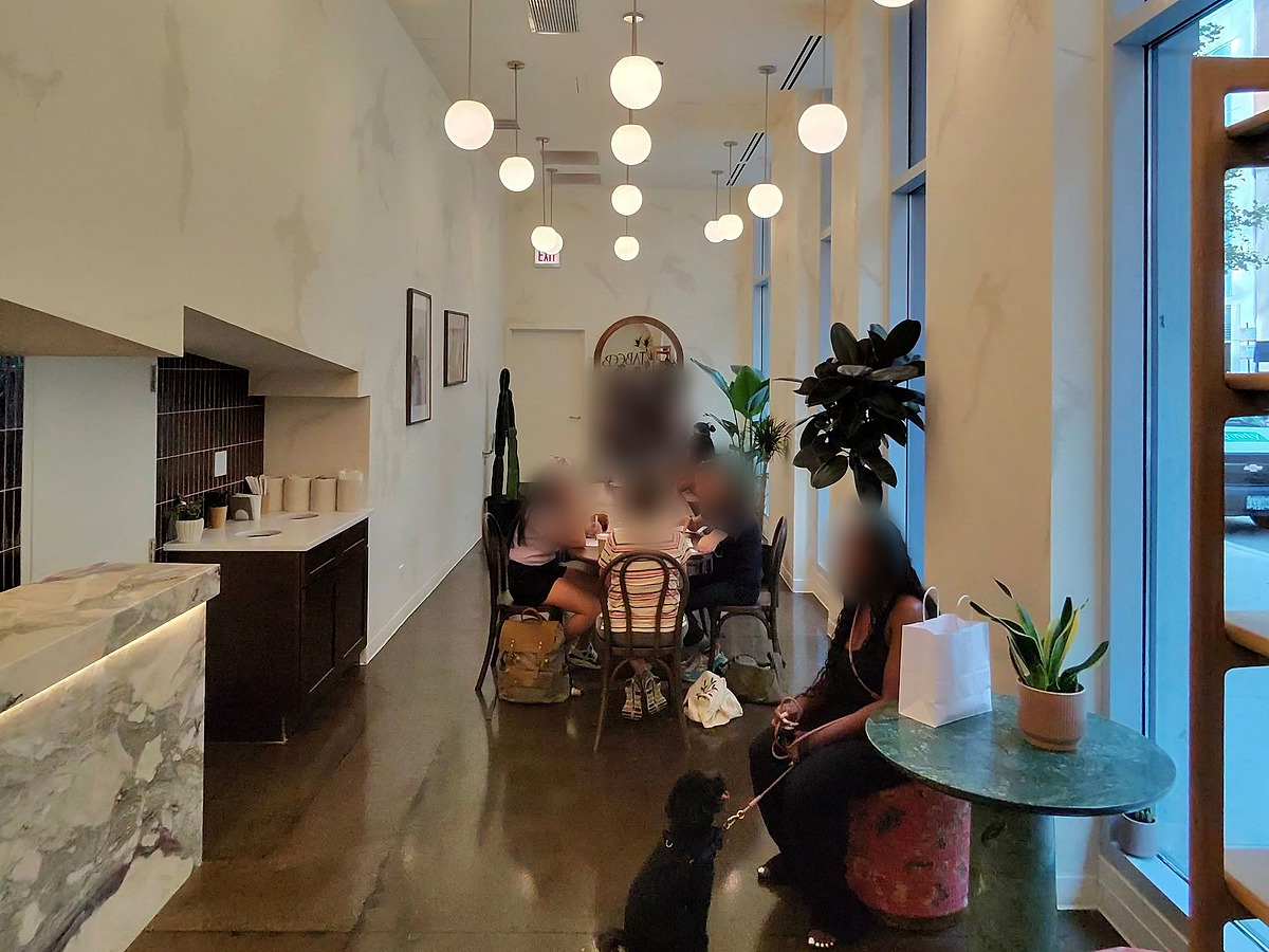 The finished cafe interior looking in from the door: the marble counter, a row of globe pendants, an arched mirror and planting