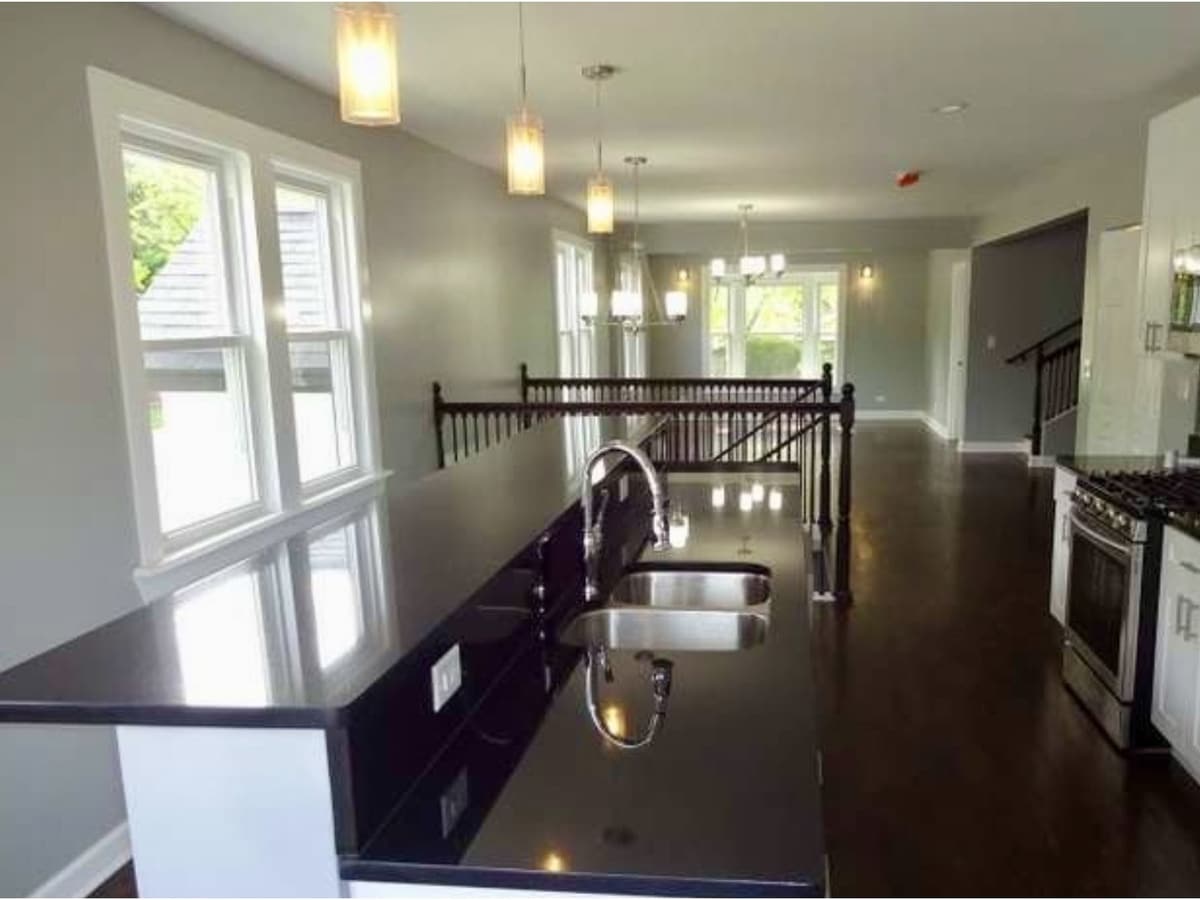 An open-plan kitchen with a dark stone counter and pendant lights, looking across a stained stair rail to a dining room beyond