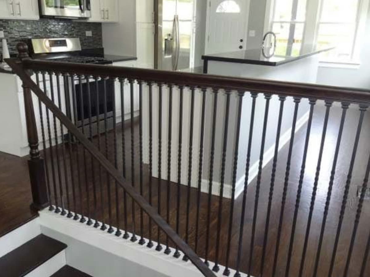 A stained hardwood stair rail with turned balusters, seen from the landing above, with dark hardwood running away from it