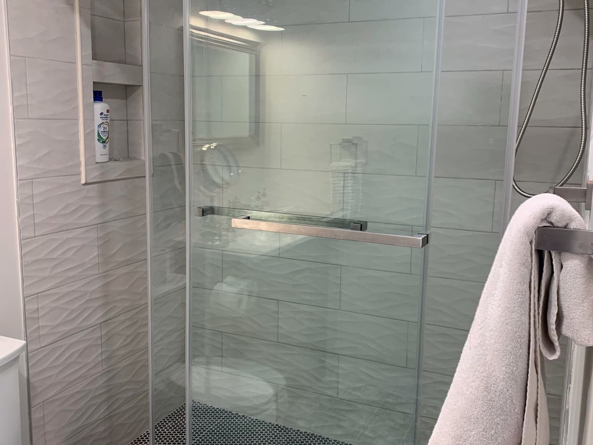 A glass shower enclosure lined in wave-textured gray tile, with a recessed niche and a dark penny-round tiled floor