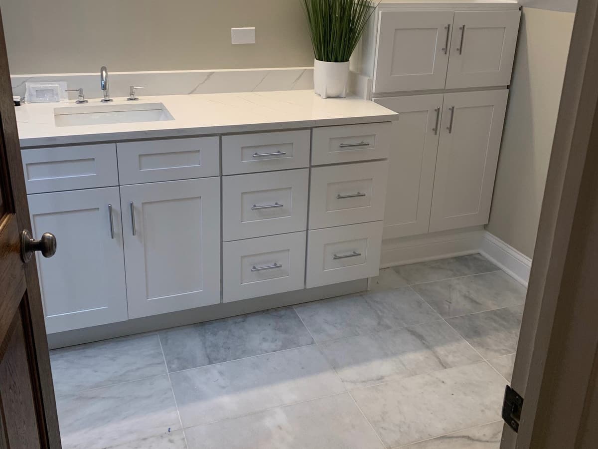 A white vanity with a marble-look top and floor, under a sloped attic ceiling