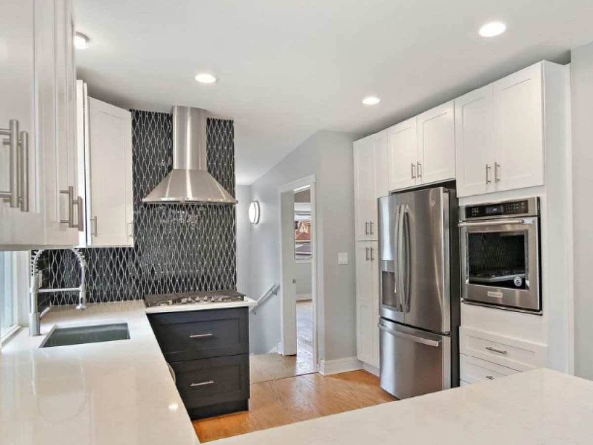 The same kitchen from the range wall, showing the hood, the geometric backsplash and a stainless fridge