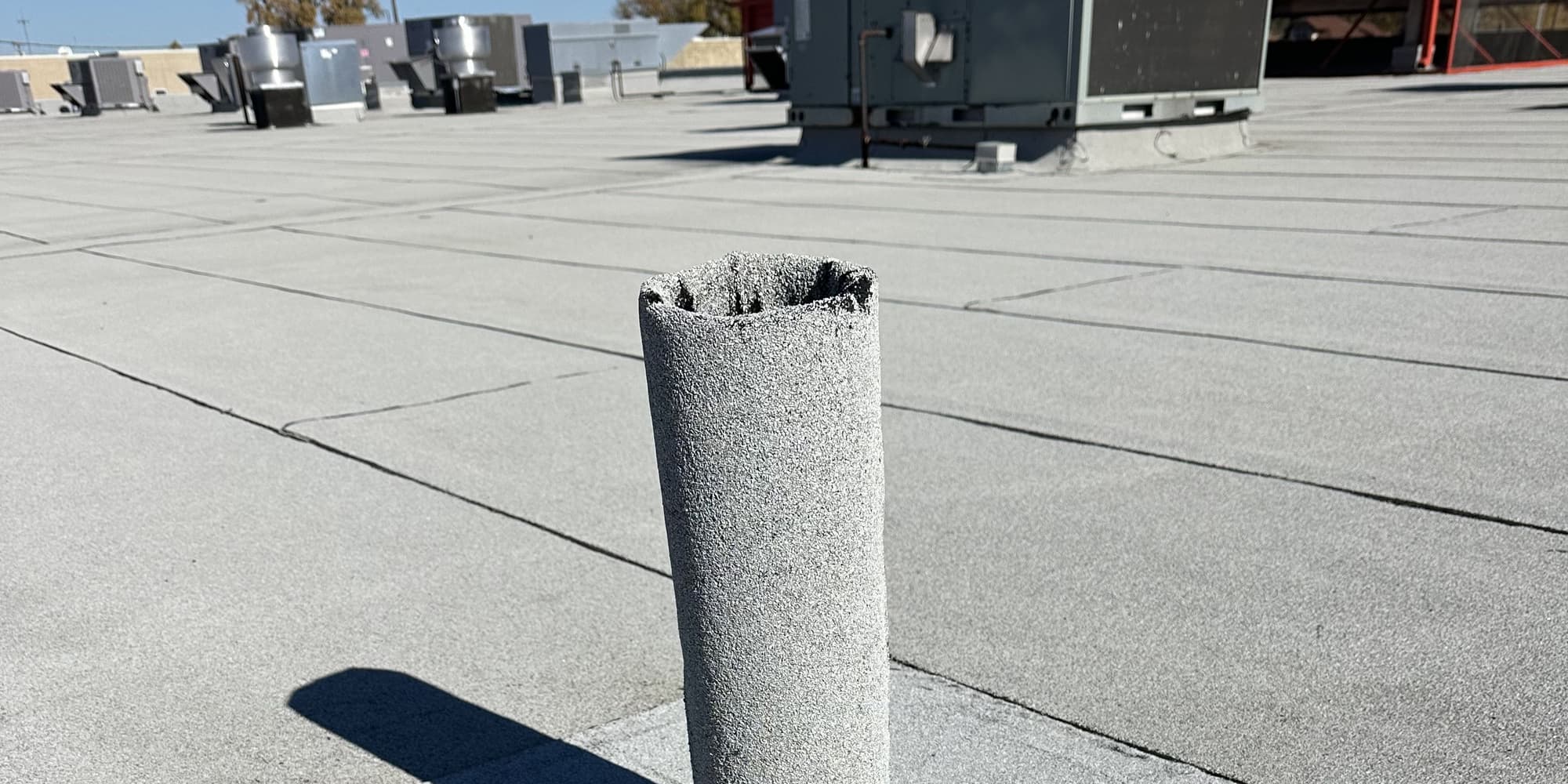 A granulated flat roof running to rooftop mechanical units, with a membrane-wrapped vent stack in the foreground