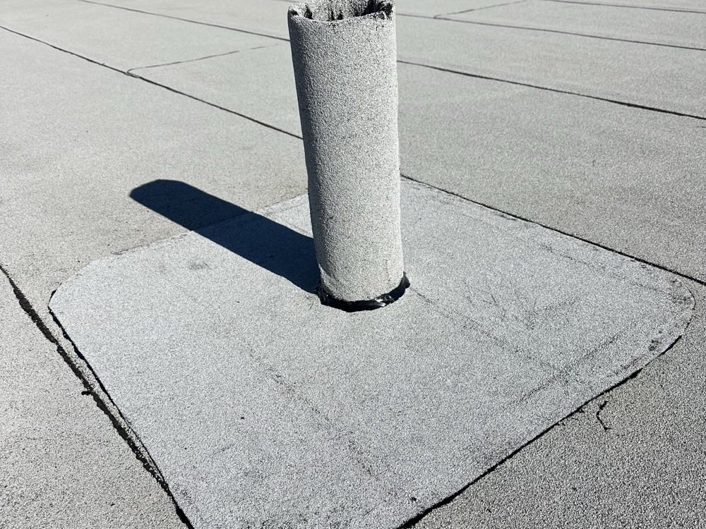 A low-slope roof surface in granular cap sheet, with a flashed pipe penetration