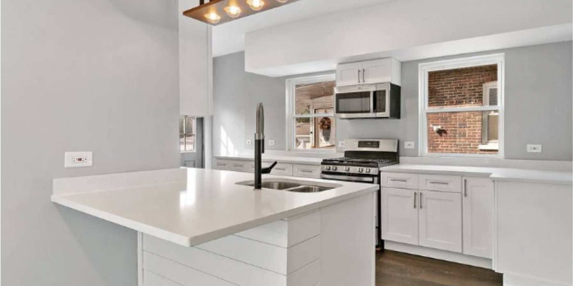 A finished kitchen with white shaker cabinets, a white quartz peninsula, a stainless range and hardwood floors